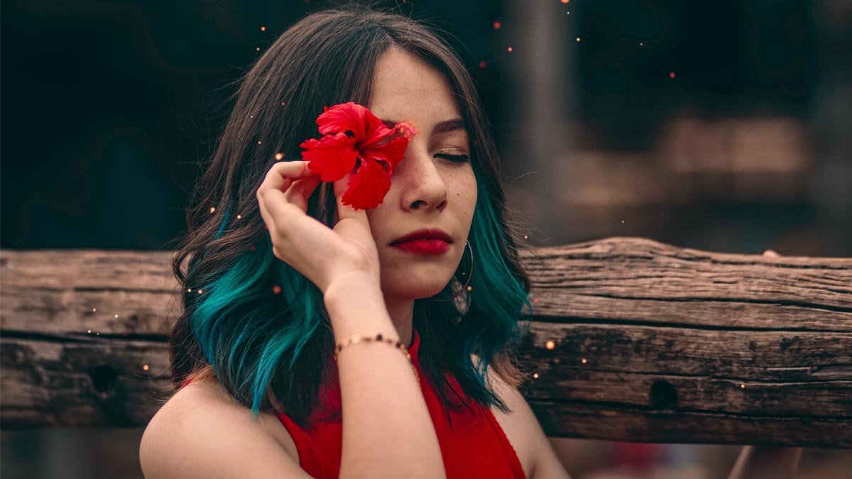 mulher com cabelo azul segurando flor vermelha